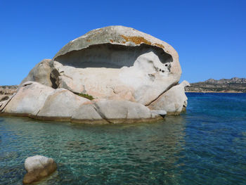 Rock formation in sea against clear blue sky