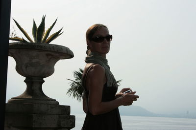 Young woman wearing sunglasses standing against sky