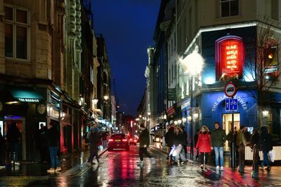 People walking on wet street in city at night