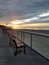 Empty bench by sea against sky during sunset