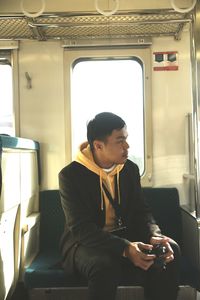 Rear view of man seated in the train looking through the window 