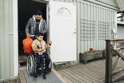 Father with backpack pushing autistic son sitting on wheelchair at doorway