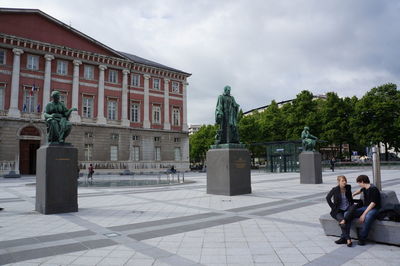 Couple sitting on seat by historic building at chambery against sky