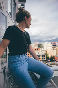 Side view of young woman sitting in city against sky