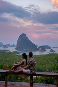 Rear view of woman sitting on mountain against sky