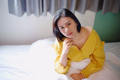 Portrait of young woman sitting on bed at home