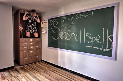 Girl looking at blackboard while kneeling in cabinet