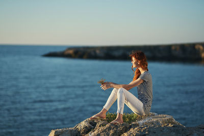 Man sitting on rock by sea against sky