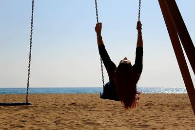 Woman swinging at beach against sky