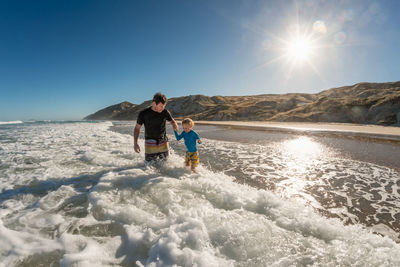 Smiling father and child playing in waves on a sunny day at a beach in new zealand