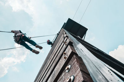 Low angle view of woman hanging on rope by building against sky