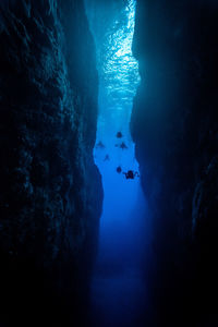 Low angle view of silhouette scuba divers swimming amidst rock formations in sea