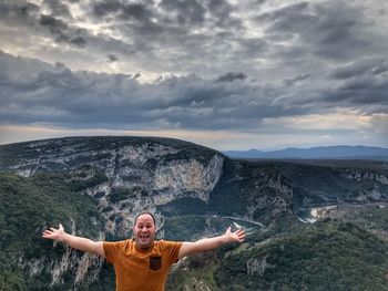 Portrait of mid adult man with arms outstretched standing on observation point against mountains