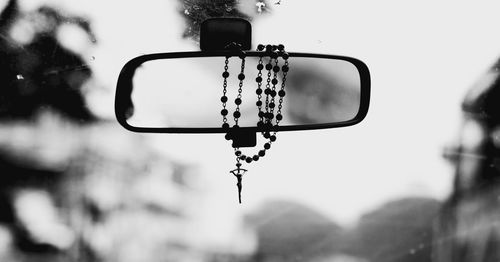 Close-up of rosary hanging on rear-view mirror in car