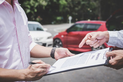 Midsection of man signing on document while agent pointing outdoors