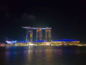 Illuminated city by river against sky at night