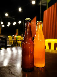 Two bottled of drinks on a table in a restaurant at night.