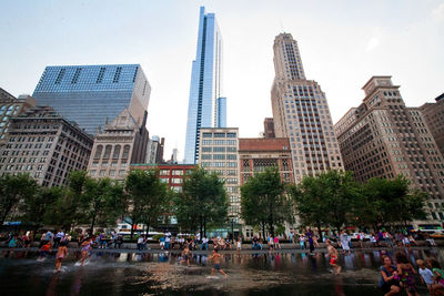 People at millennium park against buildings in city