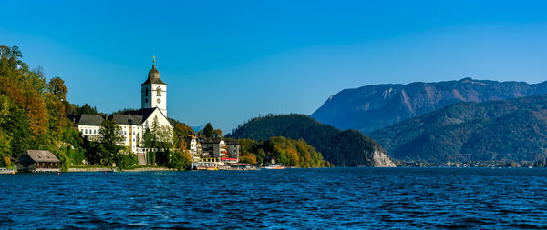 Scenic view of buildings by mountains against blue sky