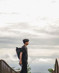 Man standing by railing against sky