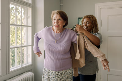 Smiling female nurse helping senior woman in wearing sweater at retirement home