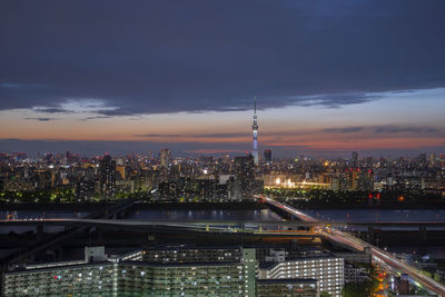 Illuminated buildings in city against cloudy sky