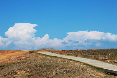 Scenic view of road amidst field against sky