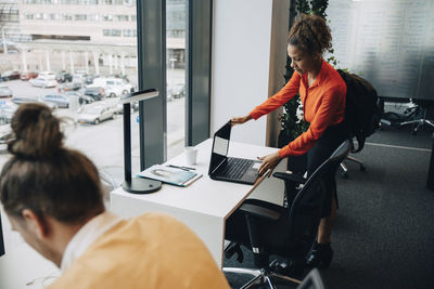 Businesswoman looking at laptop while male colleague working in office