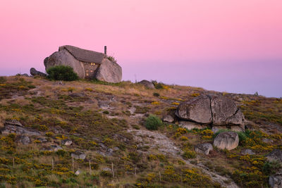 Old building on rock against sky during sunset