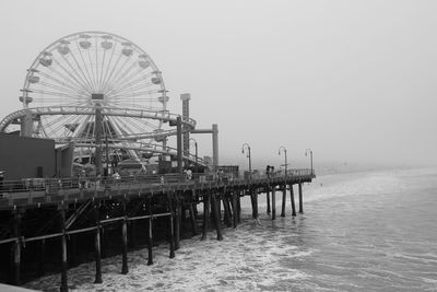 Amusement park on pier over sea against sky during foggy weather