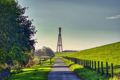 Footpath amidst trees on field against sky