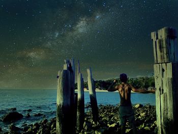 Rear view of shirtless man looking at sea against starry sky