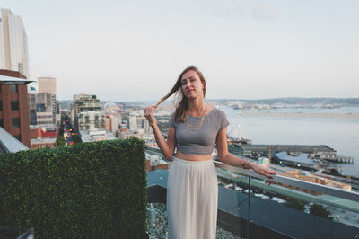 Portrait of young woman standing in city against sky