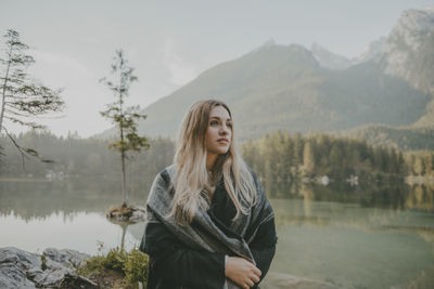 Young woman standing by lake against sky