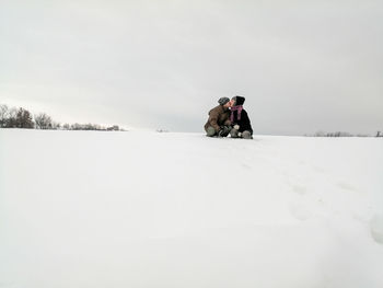 Rear view of people, kissing, on snow covered field against sky