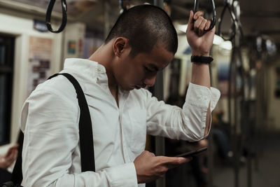 Side view of man using smart phone standing in train