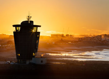 Tower on beach by buildings against sky during sunset