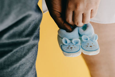 Midsection of couple holding baby booties against yellow background