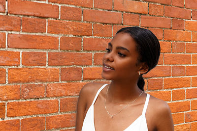 Close-up of woman looking away while standing against brick wall