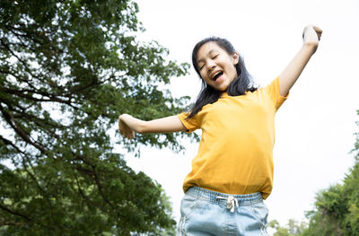 Low angle view of young woman standing against trees