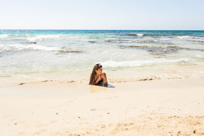 Woman sitting on shore at beach against sky