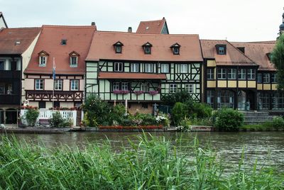 Buildings in front of river and grass against sky at bamberg