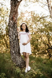 Smiling pregnant woman standing by tree on grassy field