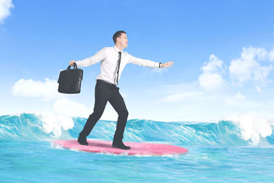 Smiling businessman with bag standing on surfboard in sea