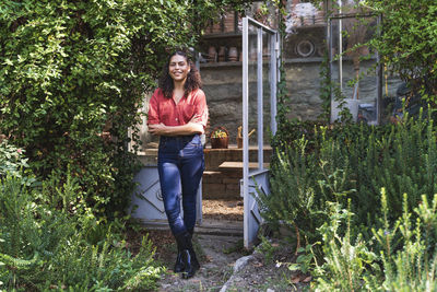 Woman with arms crossed standing in back yard on sunny day