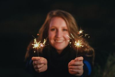 Close-up of young woman holding illuminated sparklers at night