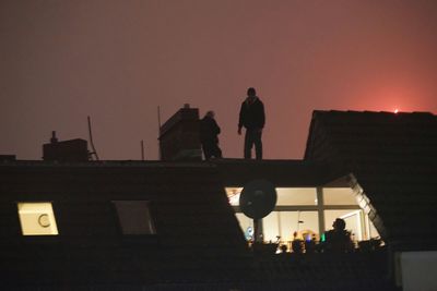 Silhouette people standing on railing at sunset
