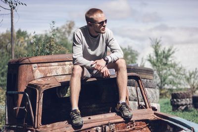 Full length of young man sitting on abandoned car