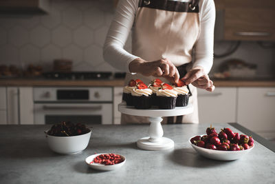 Young woman decorate cupcakes with fruits and cream cheese closeup in kitchen. working at home. 