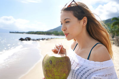 Close-up of young woman drinking fresh coconut water on the beach.